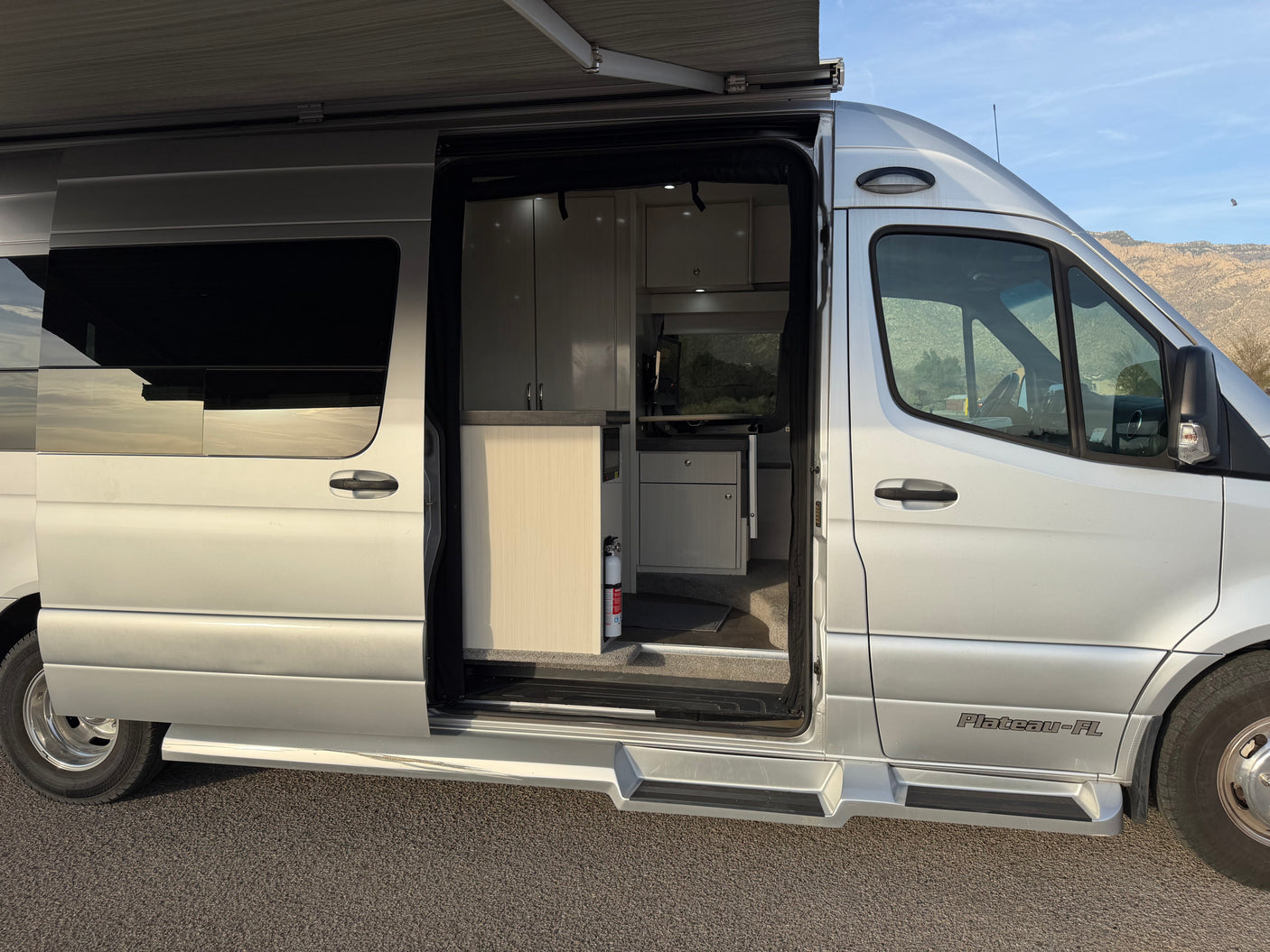 RV rental: Silver camper van with side door open, revealing the bright interior kitchen and extended awning above.