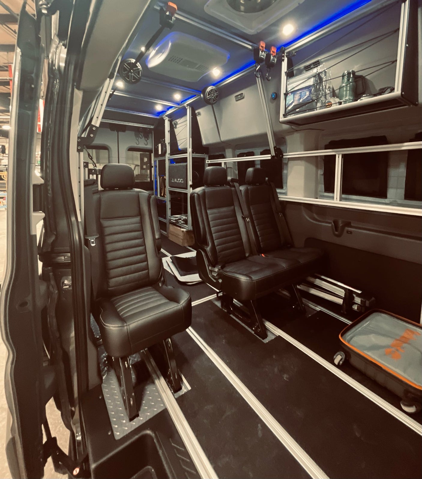 Custom van RV rental with plush black leather seating, track flooring, overhead storage, and blue LED lighting.