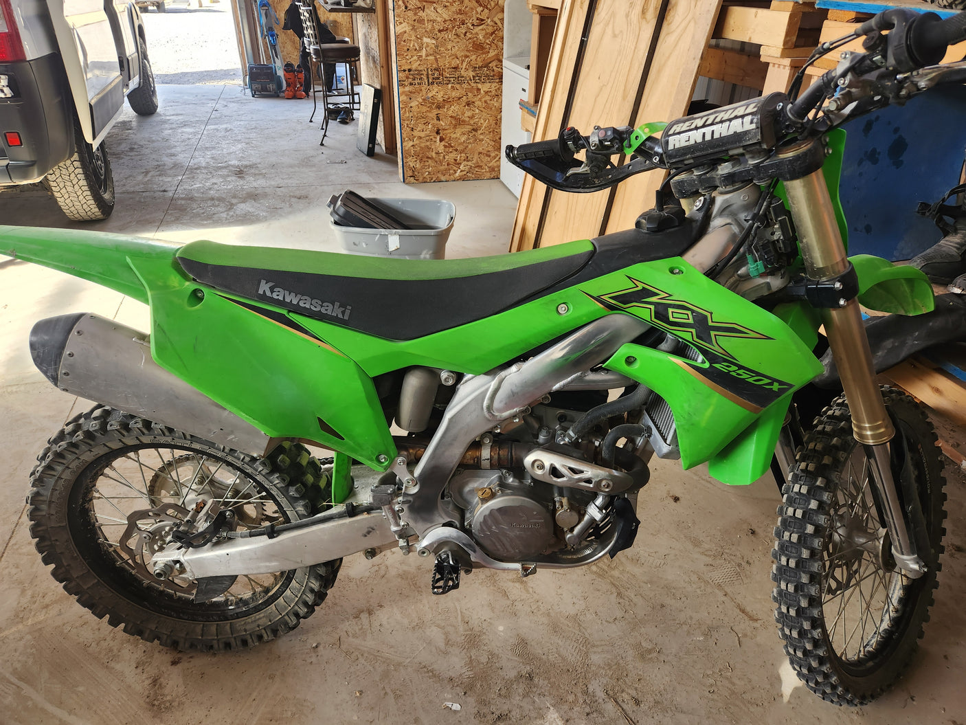 Bright green Kawasaki KX250X dirt bike, mud-splattered & ready for trails, parked inside near an RV rental.