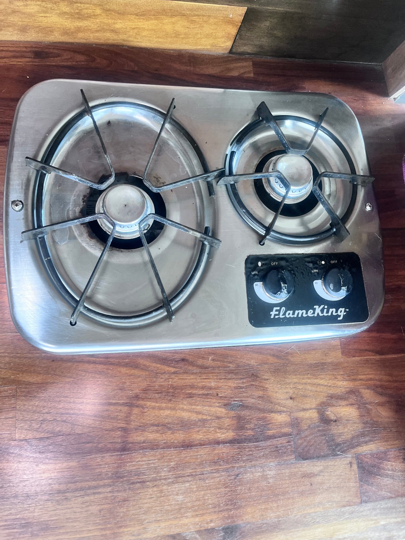 FlameKing 2-burner gas stovetop, essential for cooking in your RV rental. One burner is lit with a blue flame.
