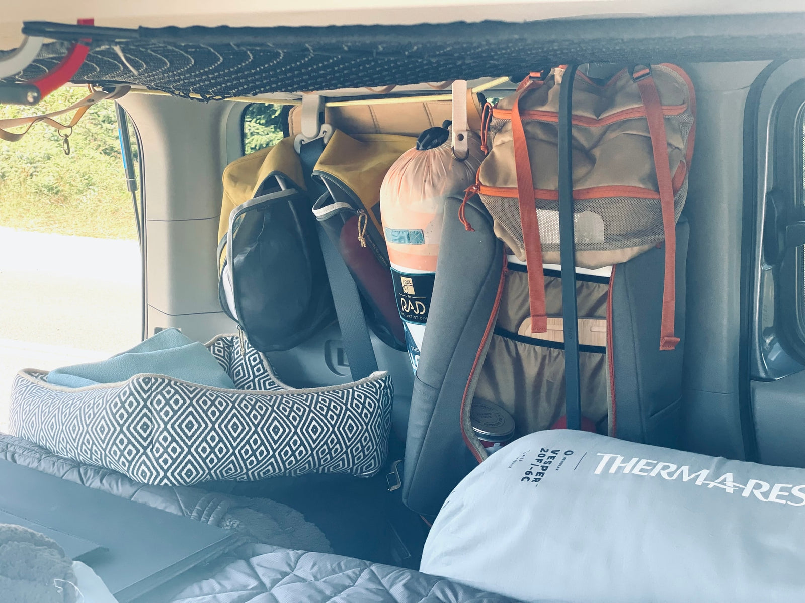 An RV rental's clever storage: overhead net, hanging bags, a dog bed, and a Therma-Rest sleeping quilt.