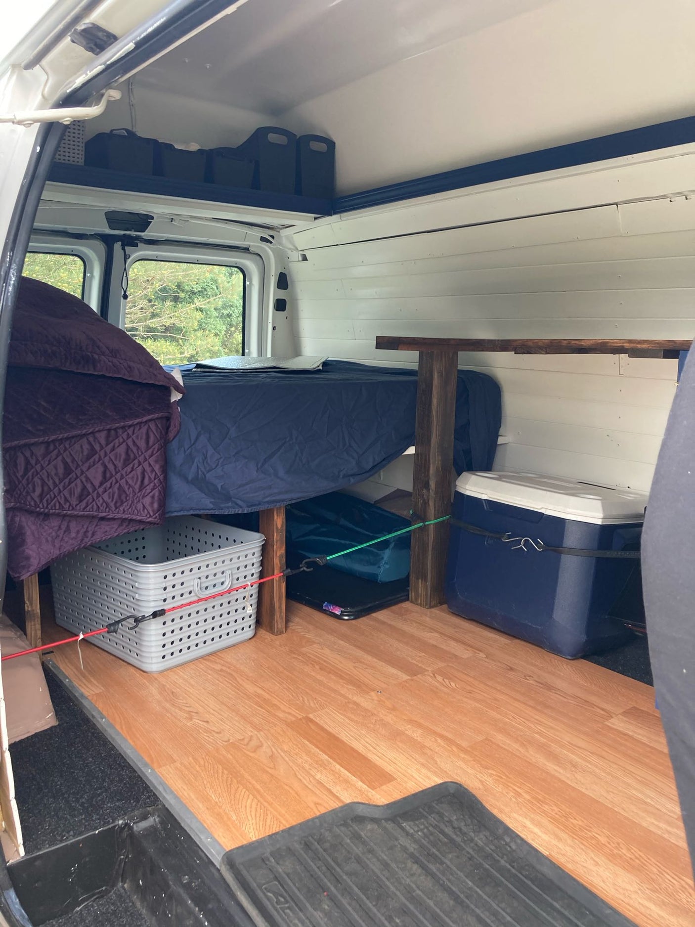Explore a compact RV rental camper van interior featuring a bed, ample storage, and durable wood-look flooring.