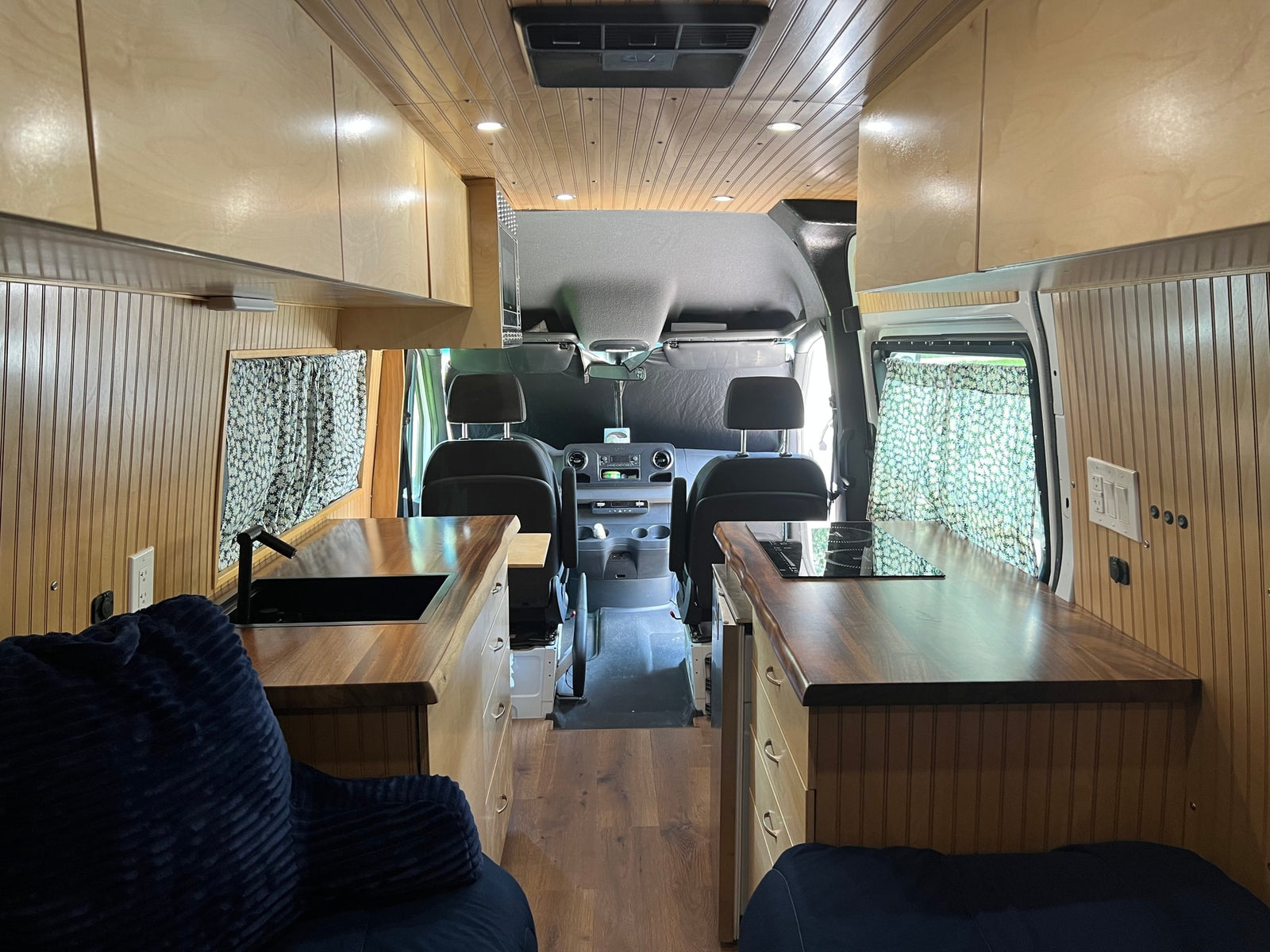 Step inside this cozy RV rental camper van with a compact kitchen, comfortable seating, and sleek wood cabinetry.