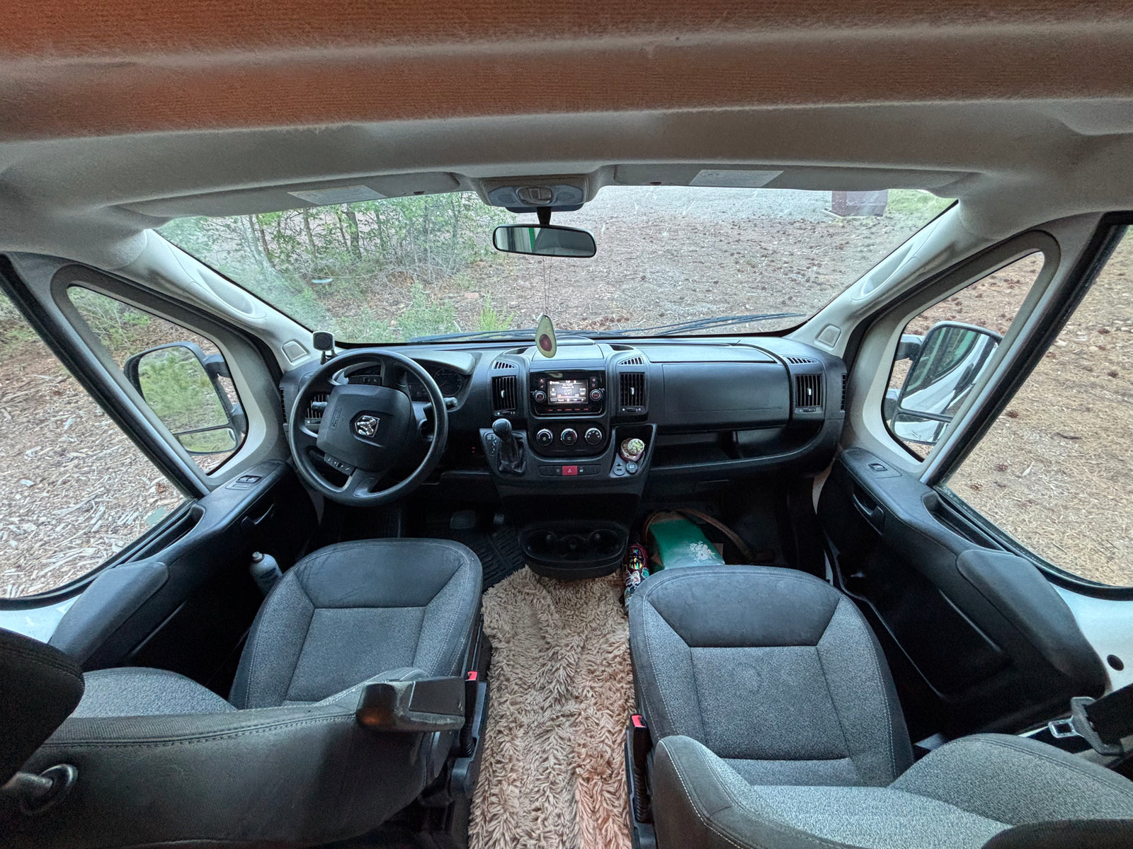 RV rental: Interior view of a van's front cabin, featuring the steering wheel, dashboard, and comfortable seats looking outside.