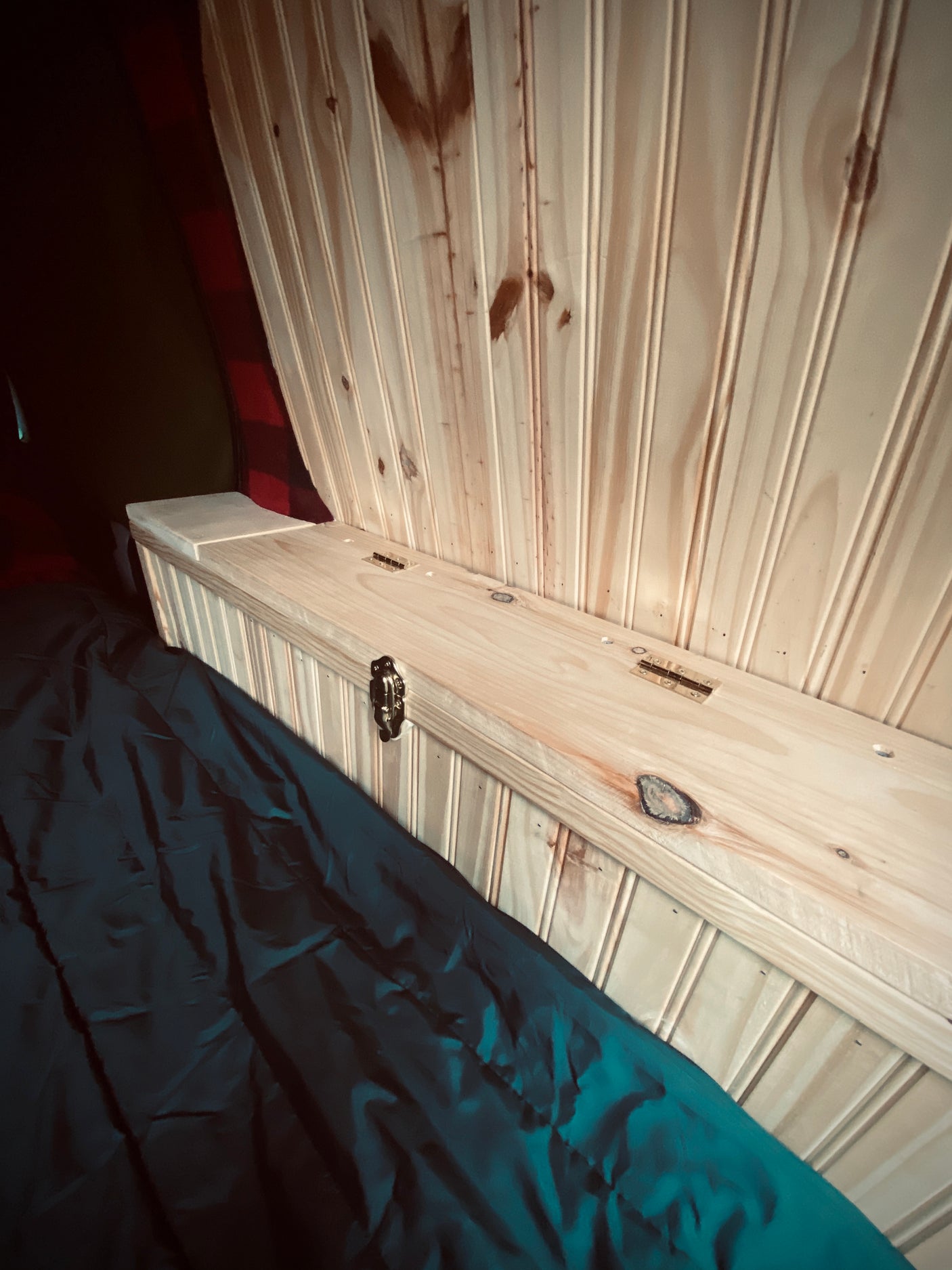 Experience this RV rental's cozy interior: light wood beadboard, hinged storage, & dark blanket on bed.