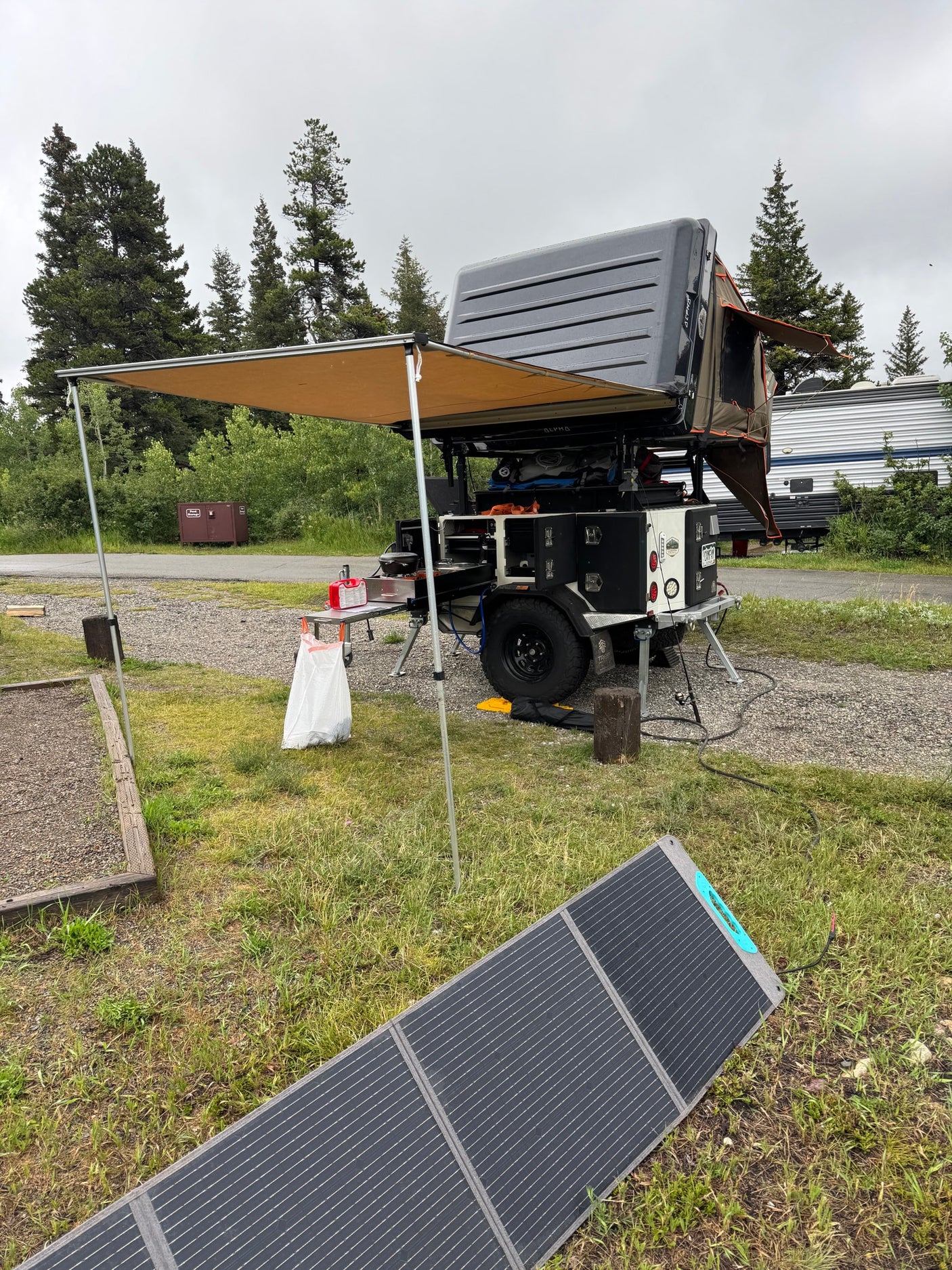 RV rental campsite setup: overland camper, awning, and portable solar panel for comfortable outdoor travel.