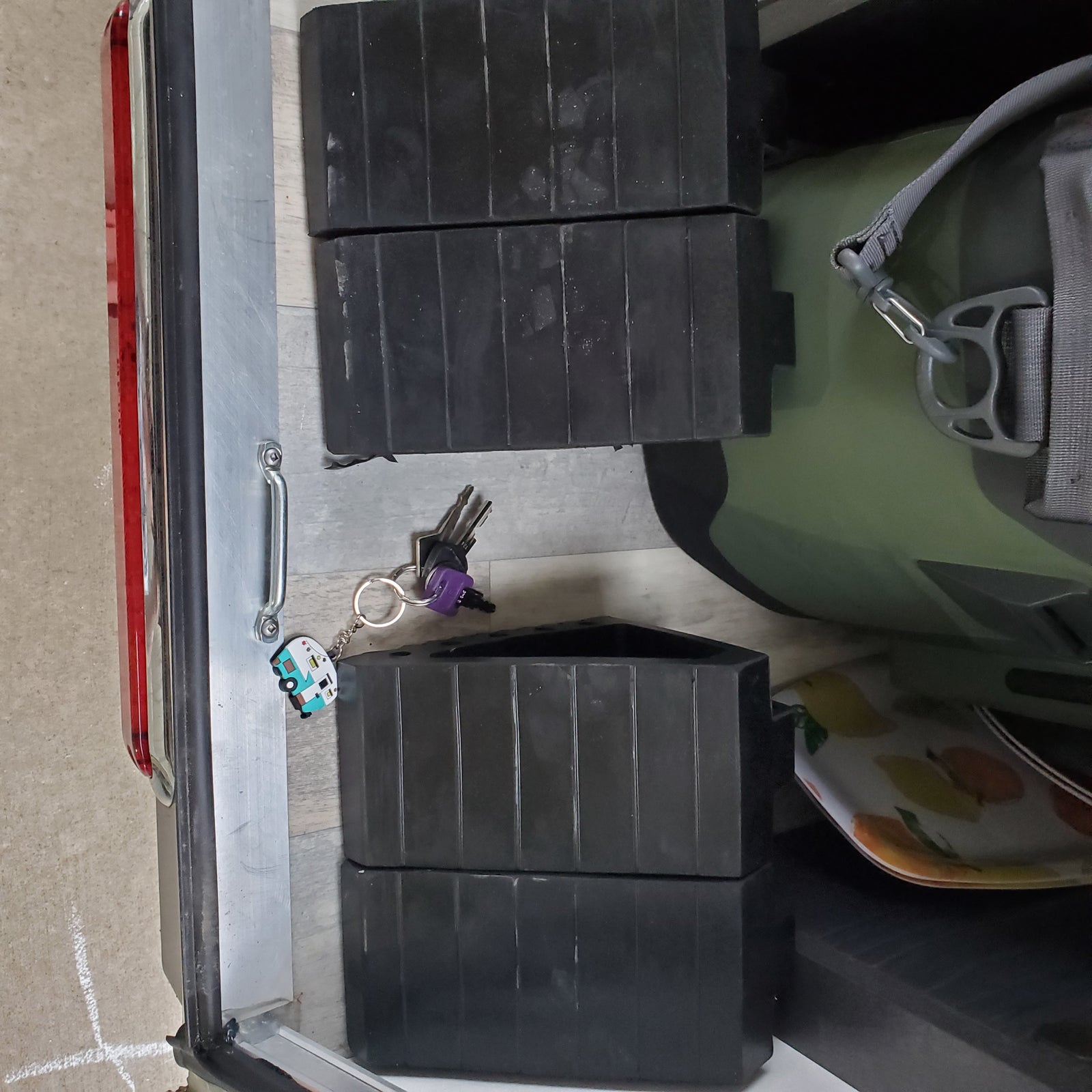 Contents for an RV rental: black leveling blocks, keys with an RV charm, and a green dry bag, neatly stored.