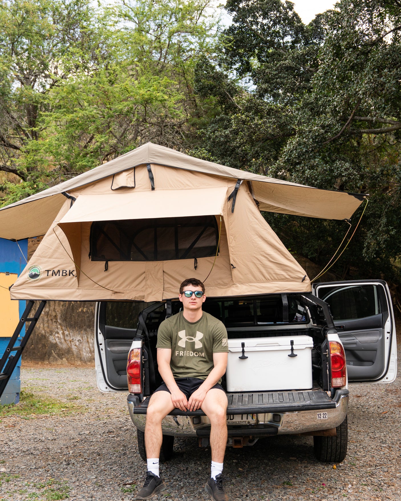 Experience outdoor adventure with this RV rental. Man on truck tailgate by a rooftop tent, perfect for camping trips.