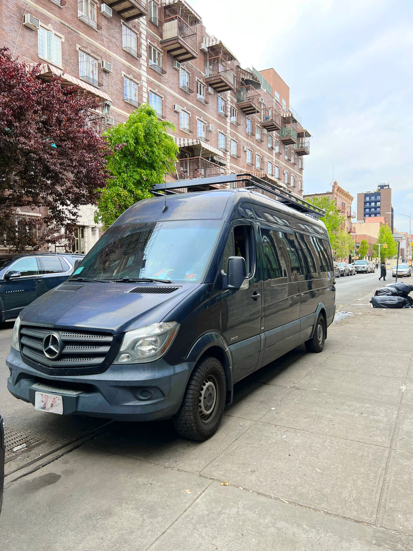 A dark blue Mercedes Sprinter van, ideal for RV rental adventures, parked on a city street with buildings.