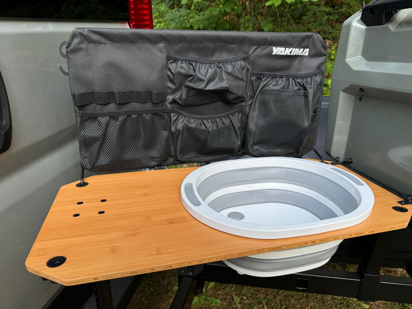 RV rental camping setup: A vehicle tailgate with a portable sink, wooden table, and fabric organizer with pockets.