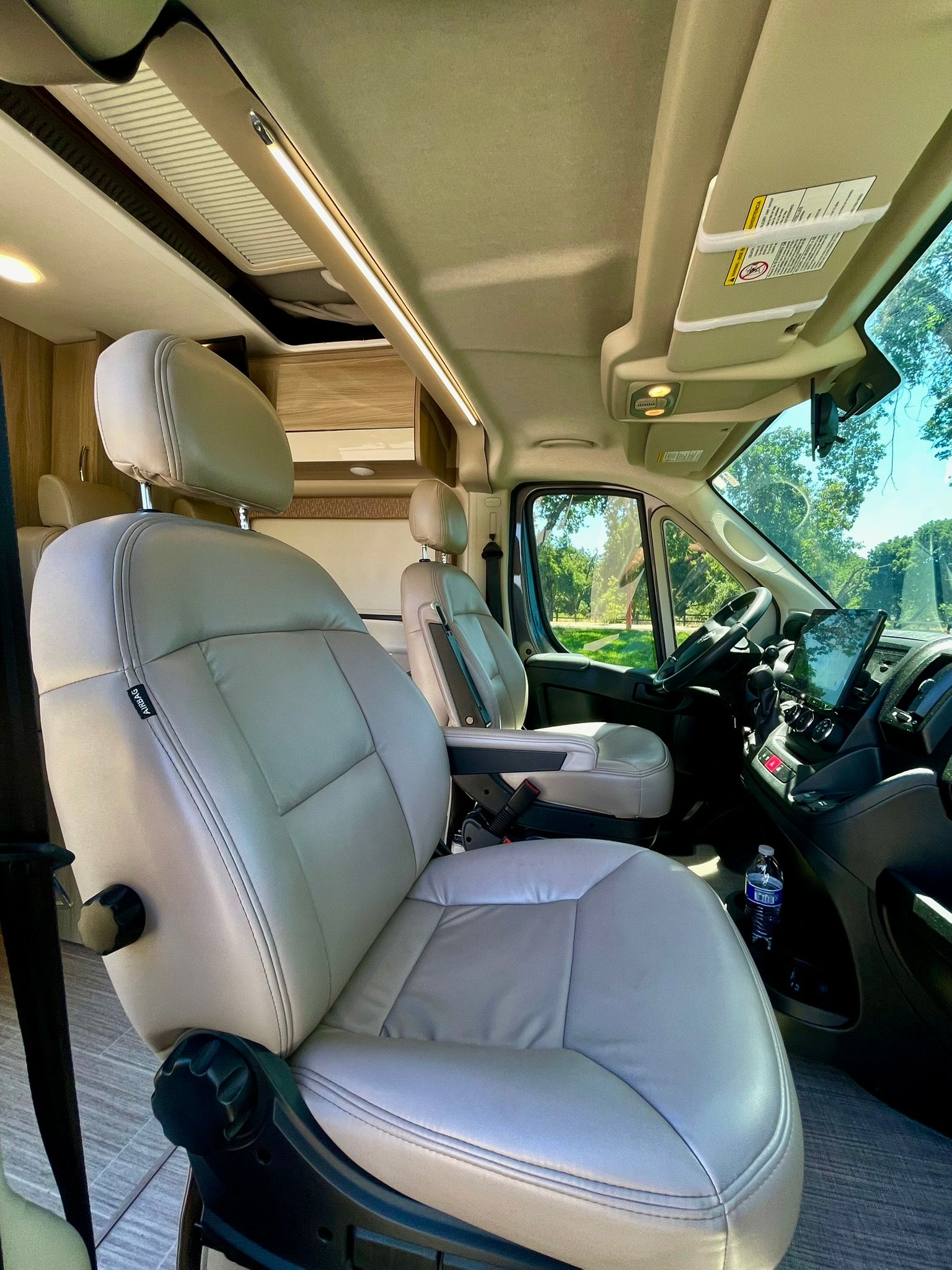 Spacious camper van RV rental interior with light leatherette seats, modern dash, and overhead lighting for travel.
