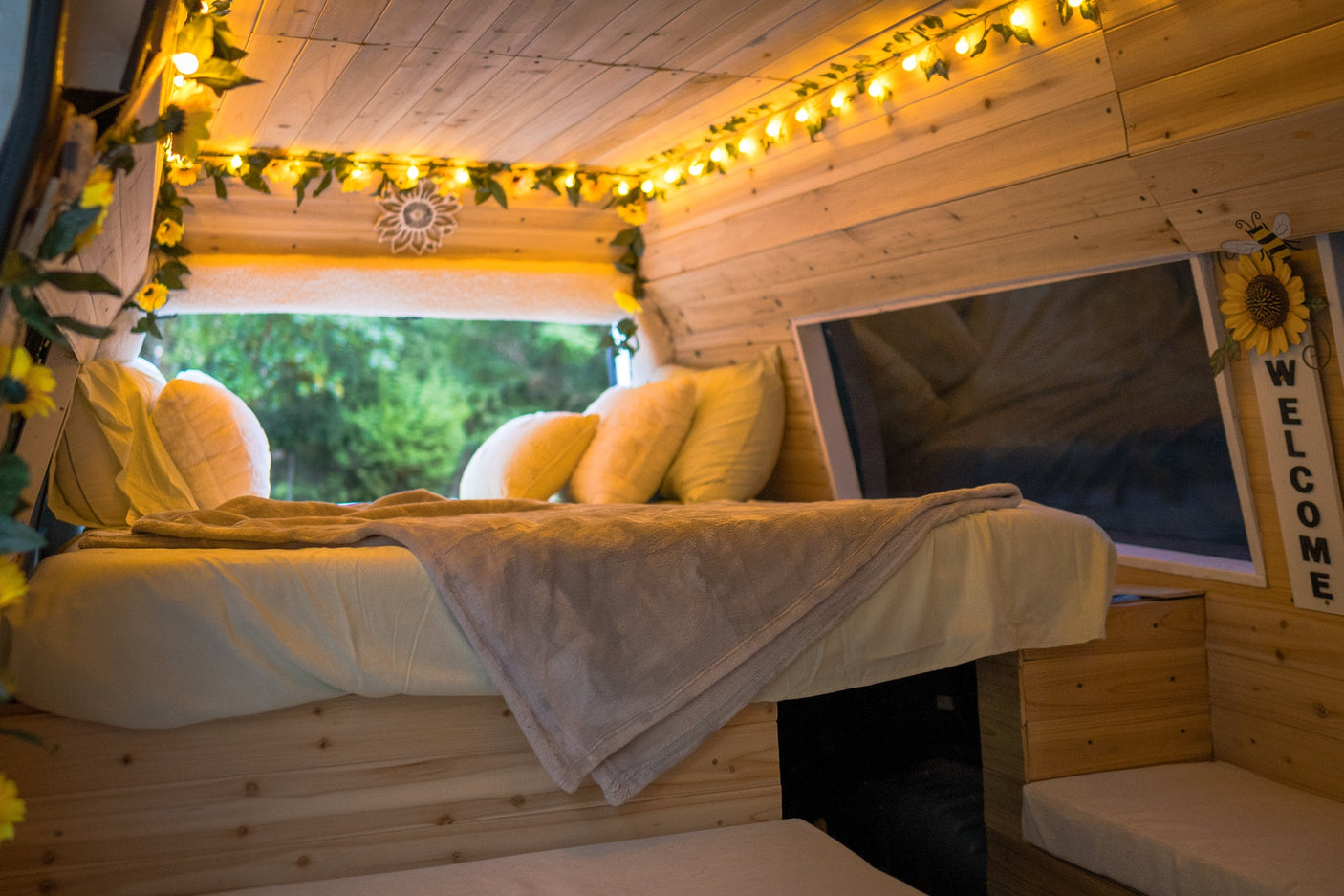 Cozy RV rental interior: bed, window view, and charming string lights on wooden walls create a welcoming retreat.