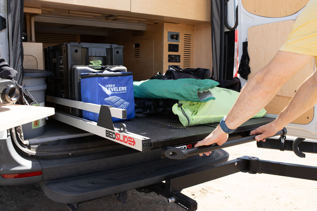 Man pulls out a BEDSLIDE from an RV rental van, showing organized storage for camping gear like Lynx Levelers.