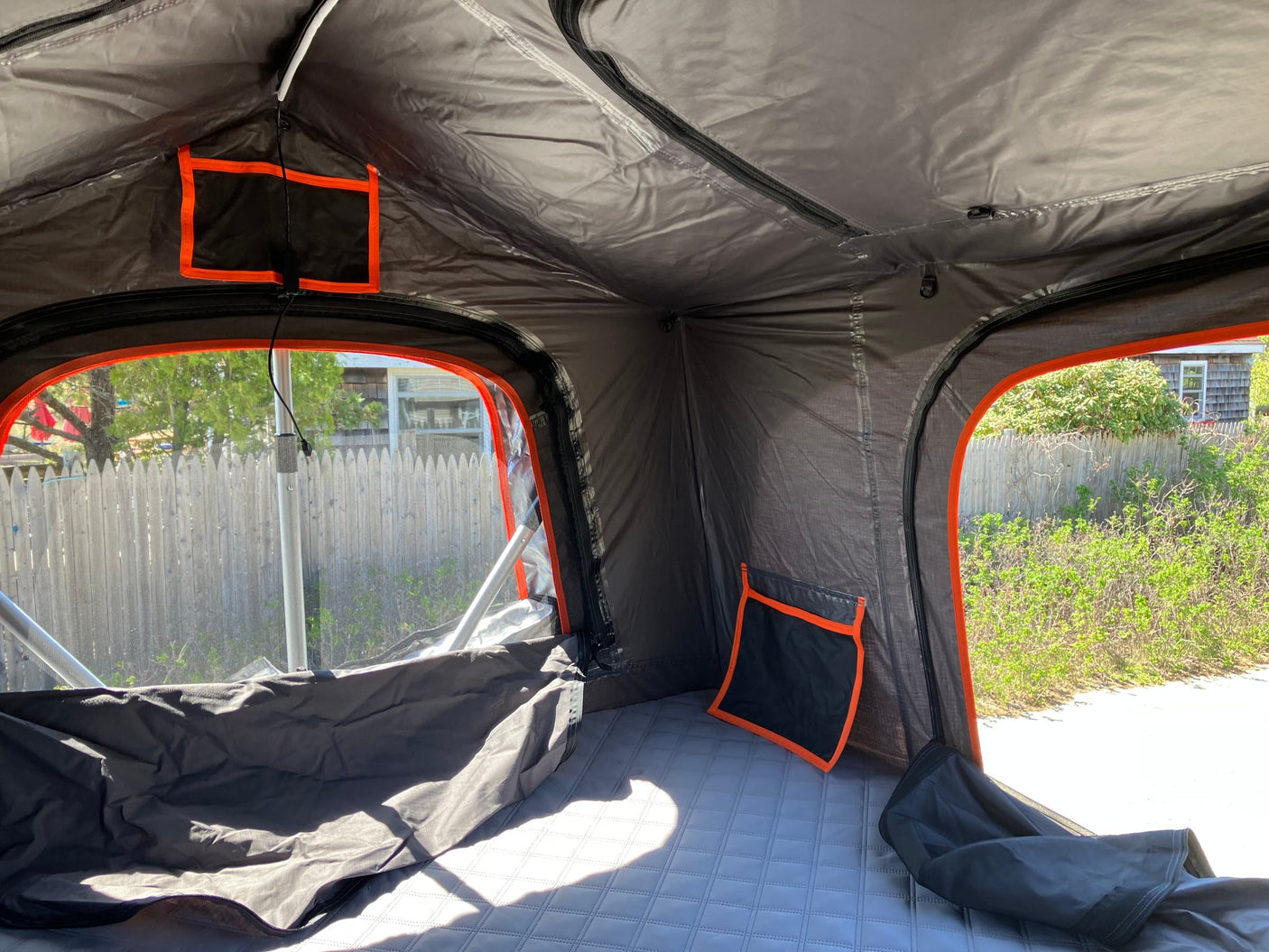 Inside a comfy RV rental tent, featuring a quilted mattress, mesh windows showing outdoor views, and handy storage.