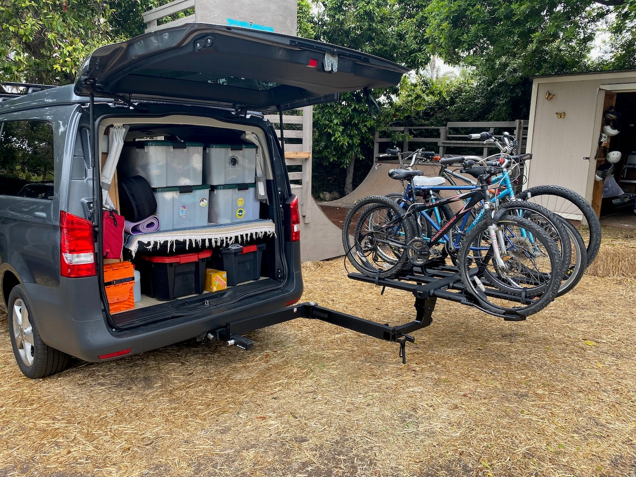 This RV rental van, tailgate open, shows organized storage bins & a yoga mat. Four mountain bikes on a hitch rack.