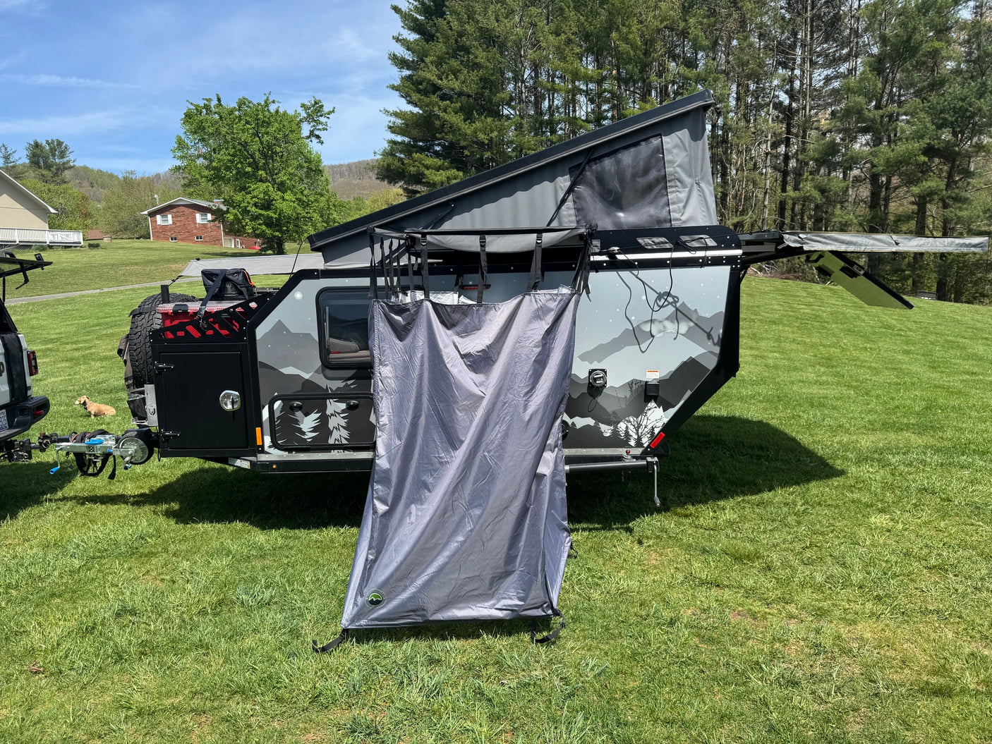 RV rental: Off-road pop-up camper trailer with privacy tent ready for adventure. Sunny day, grassy field, mountain views.
