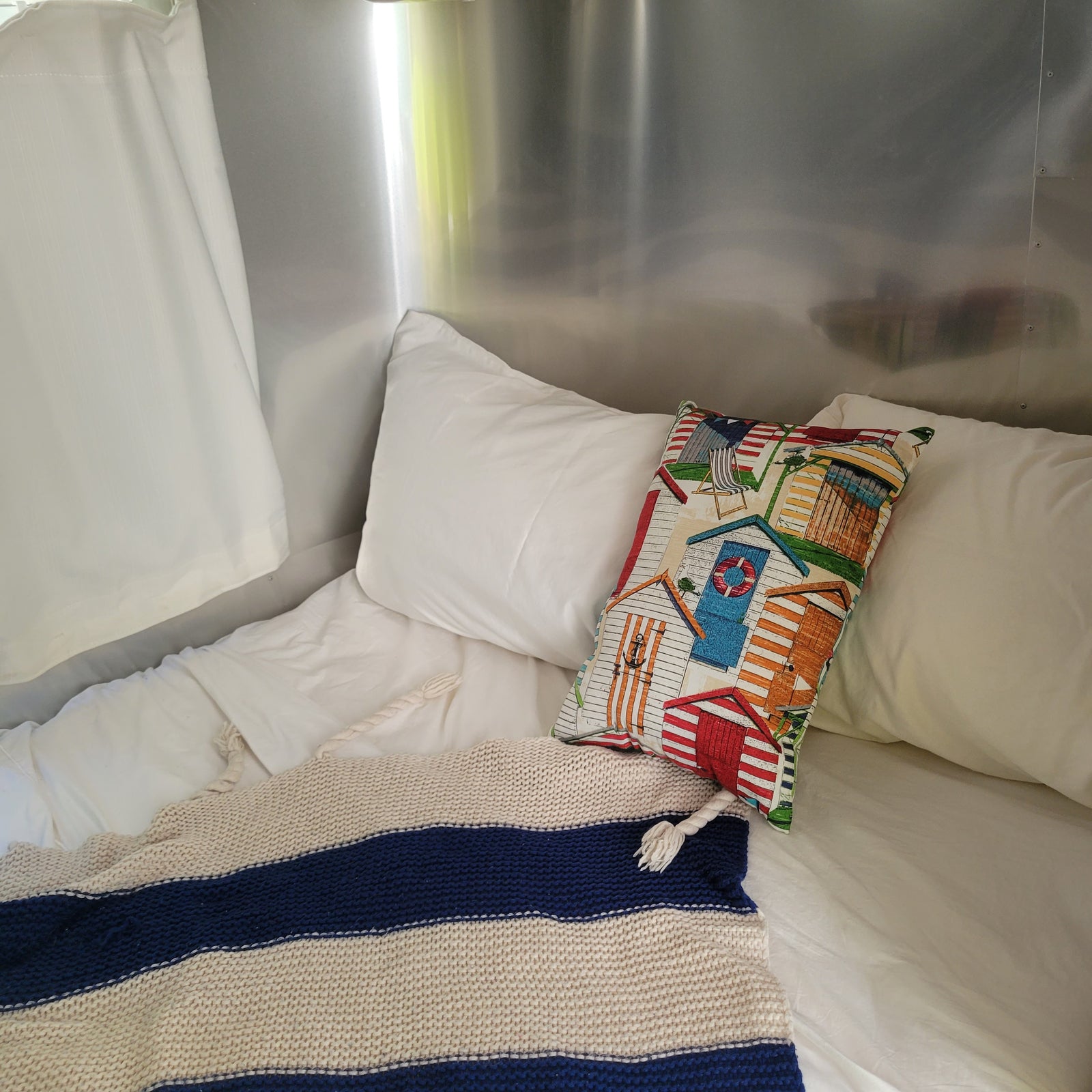 RV rental: Cozy bed with striped blanket, beach-themed pillow, and polished interior.