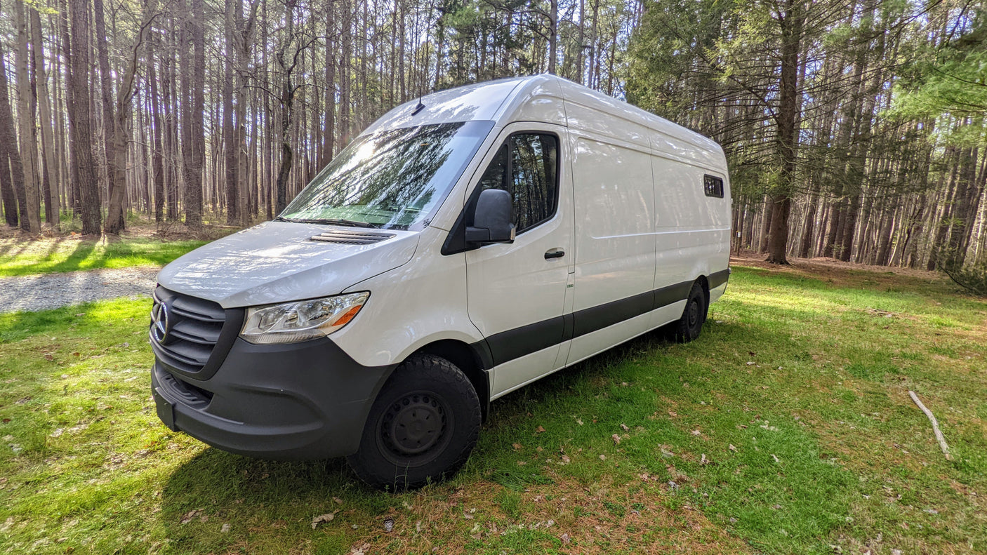 White camper van, perfect for an rv rental adventure, parked on green grass in a sunlit forest.
