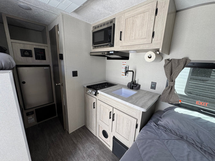 RV rental interior: compact kitchen with stove, microwave, sink, fridge, and adjacent sleeping area. Modern and functional.