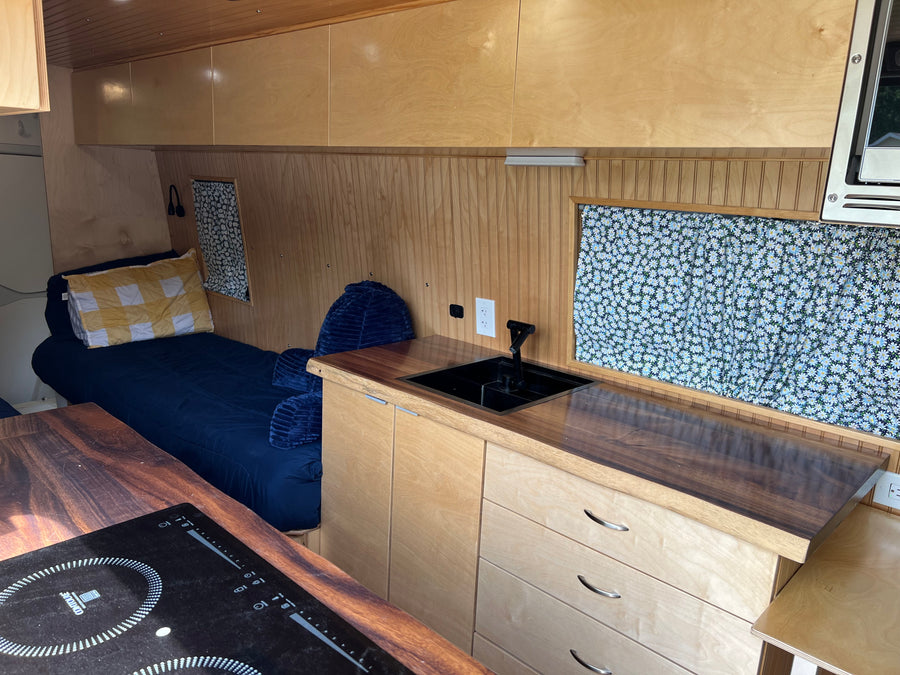 Cozy RV rental interior with a wood-accented kitchen, comfortable bed, and charming daisy window curtains.