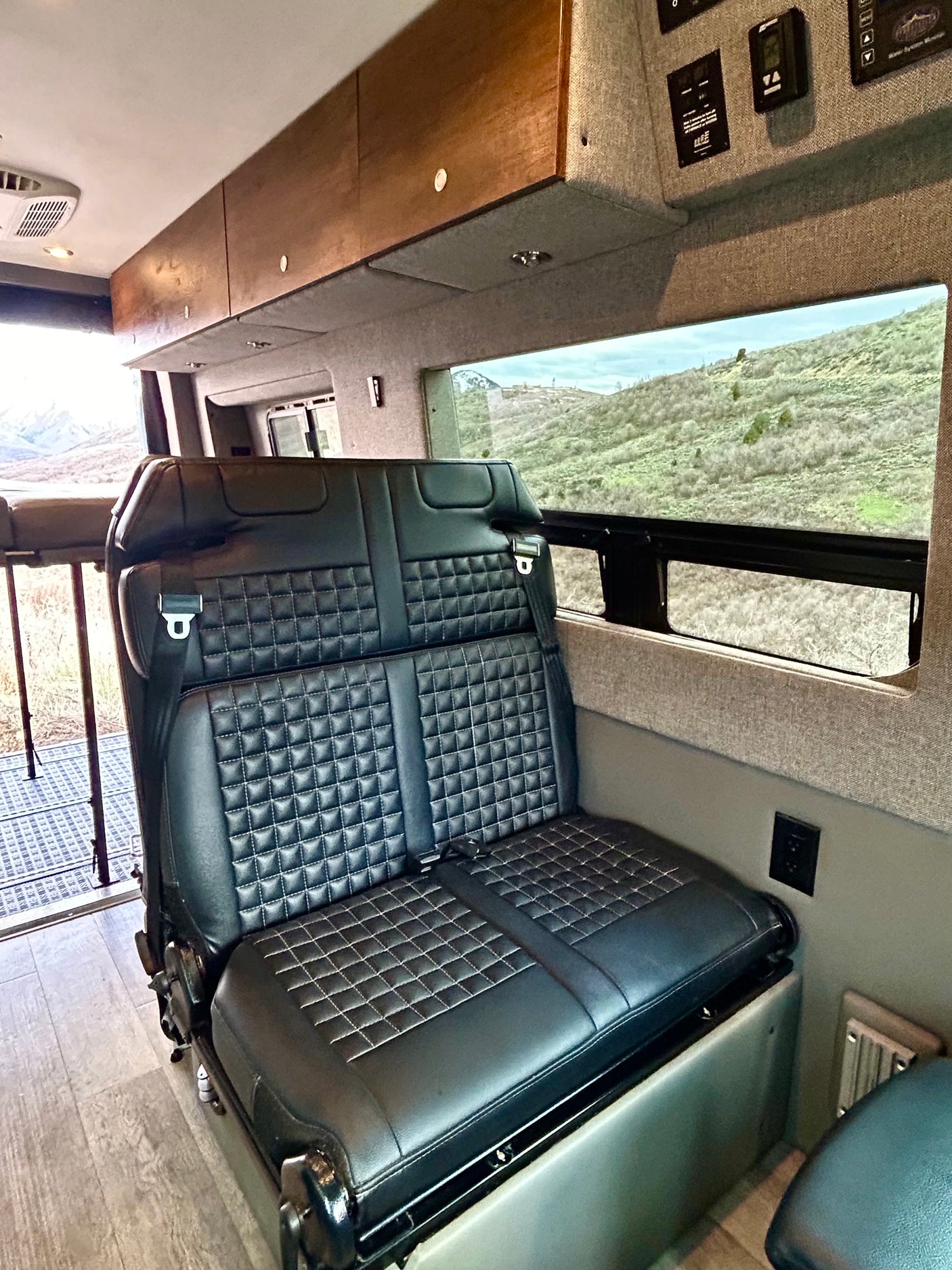 RV rental: Spacious interior featuring a comfortable black leather bench seat, overhead cabinets, and a scenic window view.