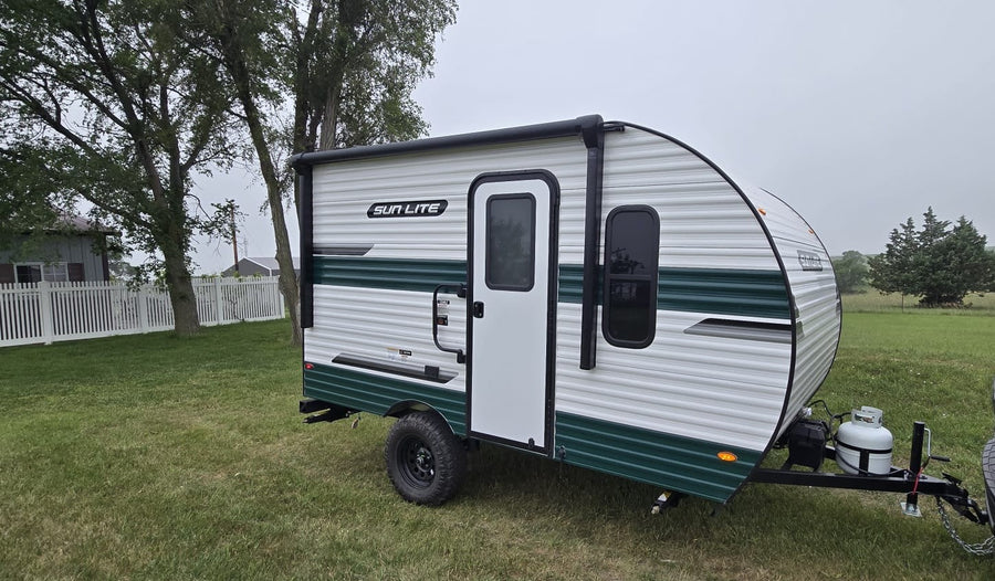 parked on grass with trees & fence background. Ready for camping!|Cream & black Sun Lite RV rental parked at a sunny vineyard