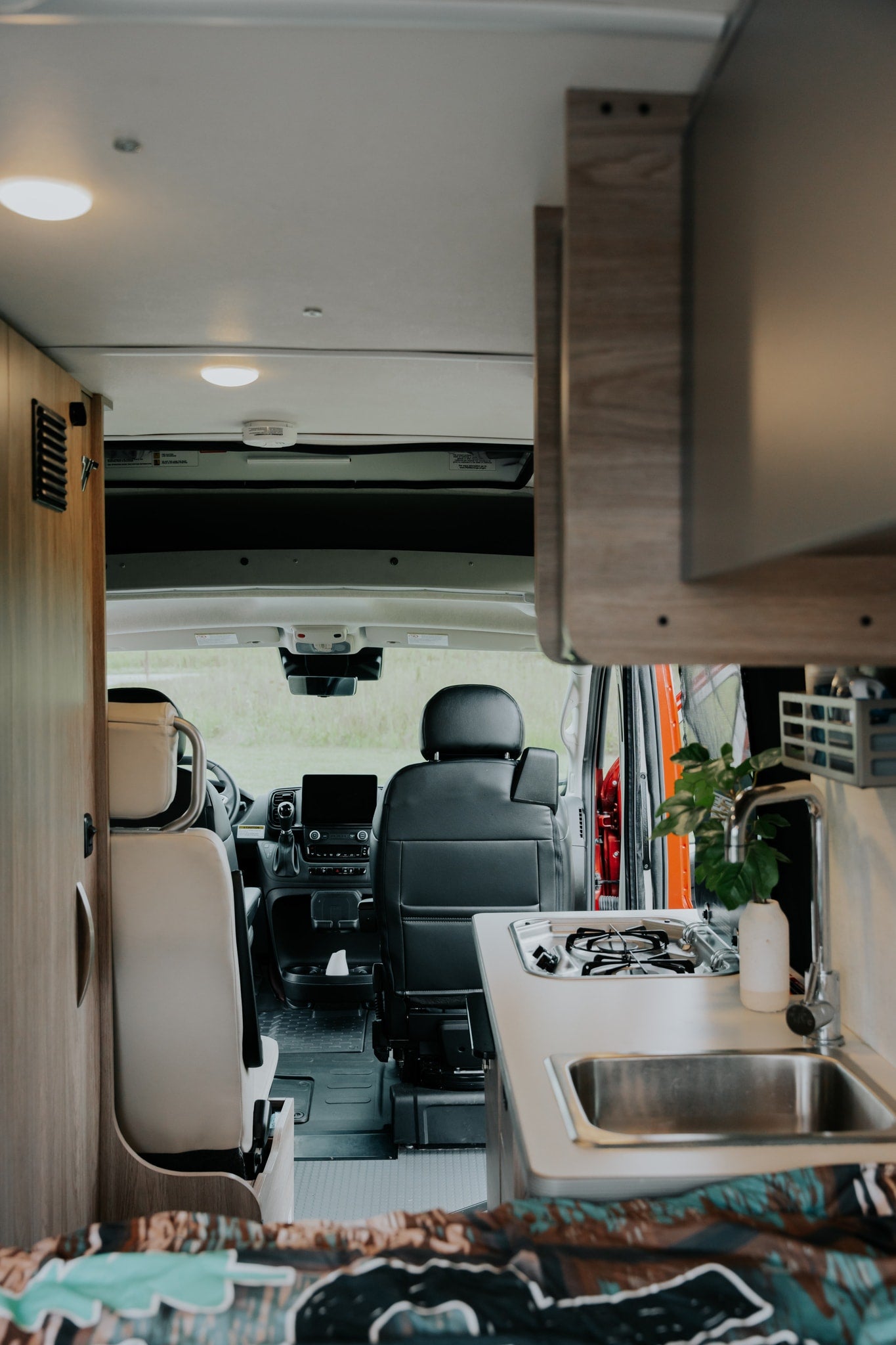 Modern rv rental interior: kitchenette with sink and stove, forward view to the camper van's cockpit and front seats.