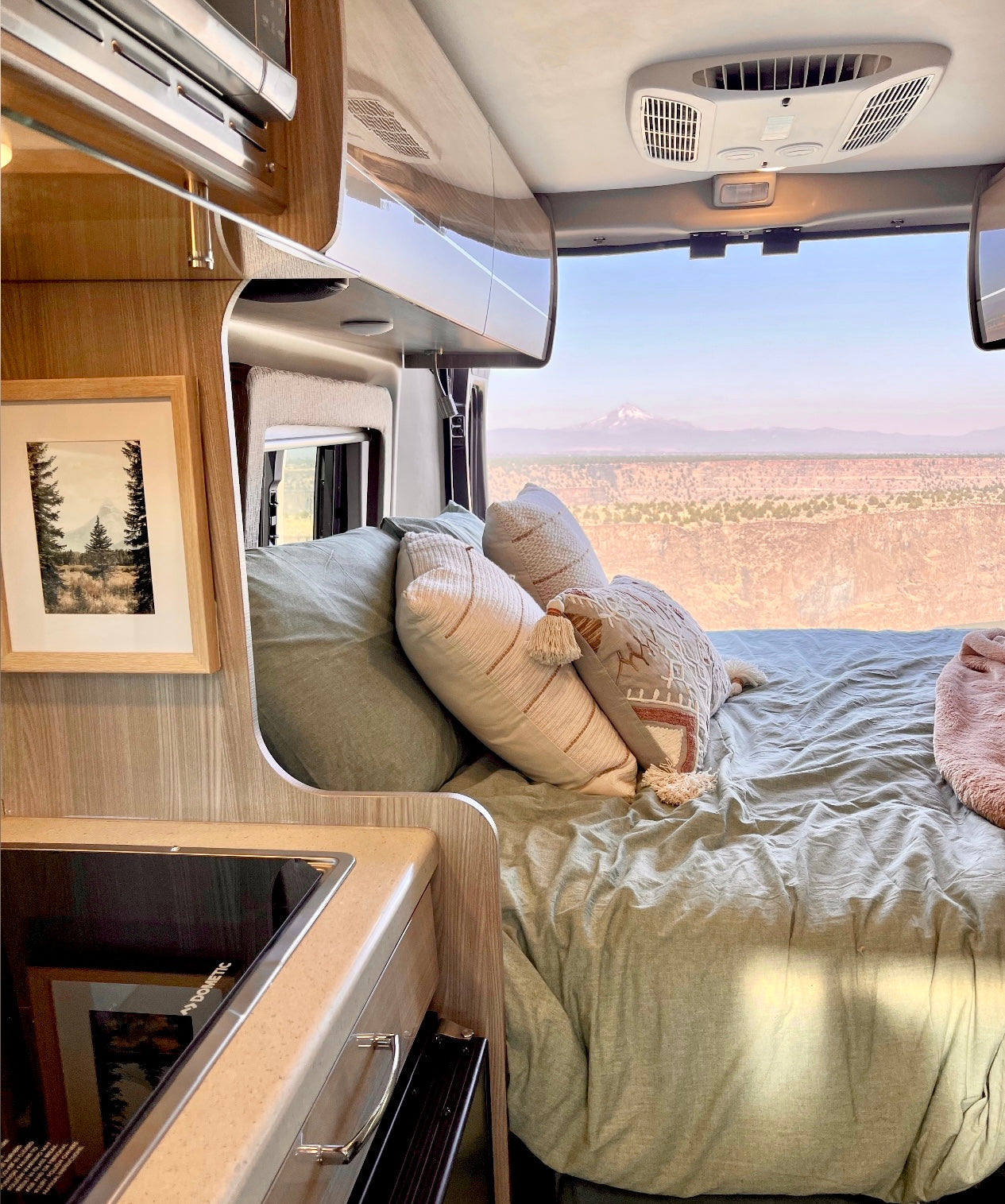 Experience an RV rental: a plush bed offers panoramic desert and mountain views. Ideal for a scenic road trip adventure.