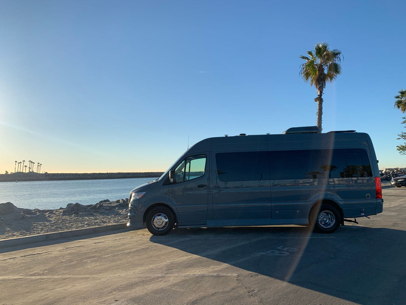 side door open. Embrace the open road.|This dark grey RV rental van is parked on a sunny day by a sandy beach and calm water. Ideal for coastal adventures!|This sleek gray Mercedes Sprinter camper van is a premium rv rental — photo 7