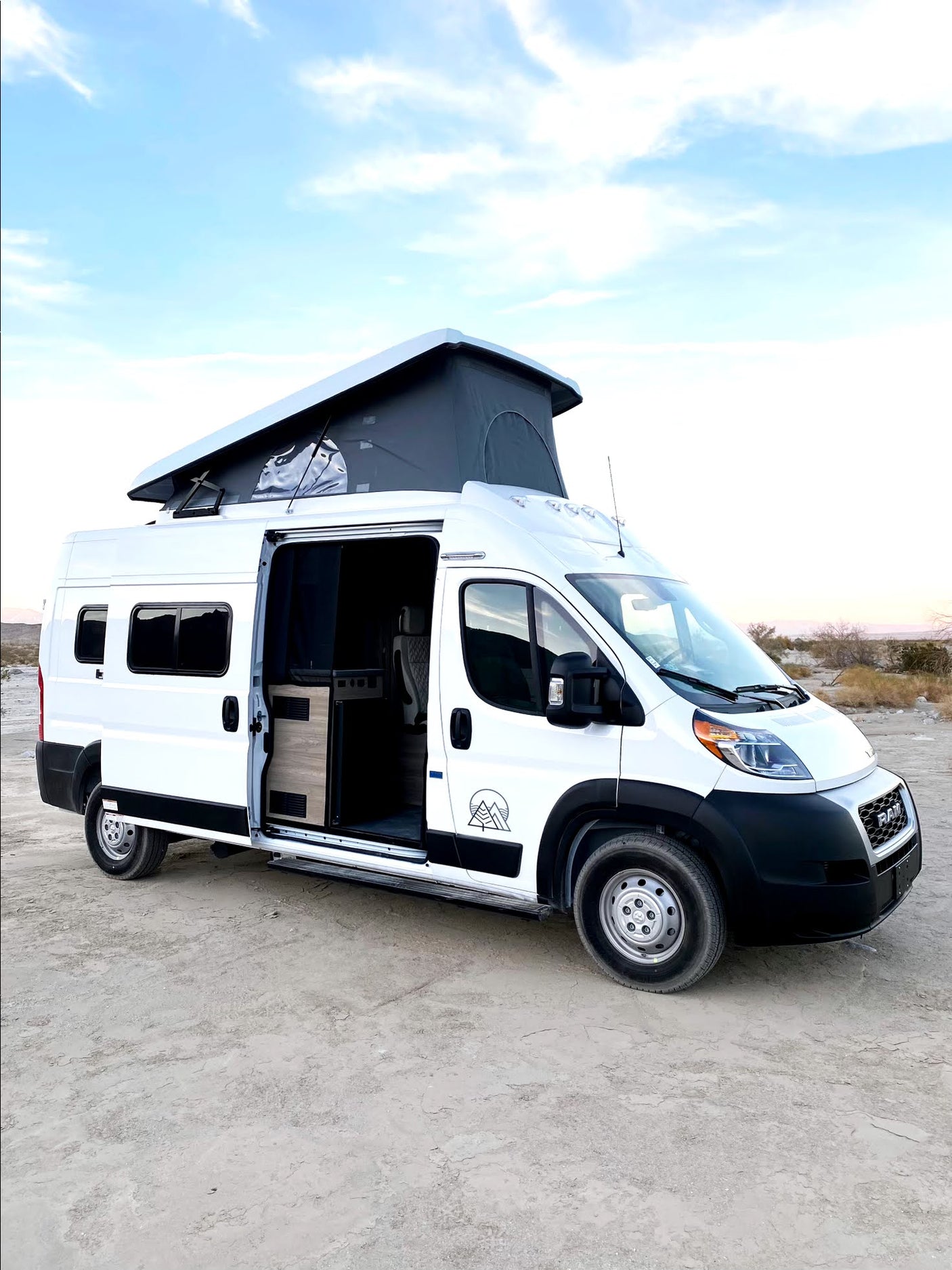 White pop-top camper van parked in a desert for rv rental adventures. Side door open, revealing cozy interior.