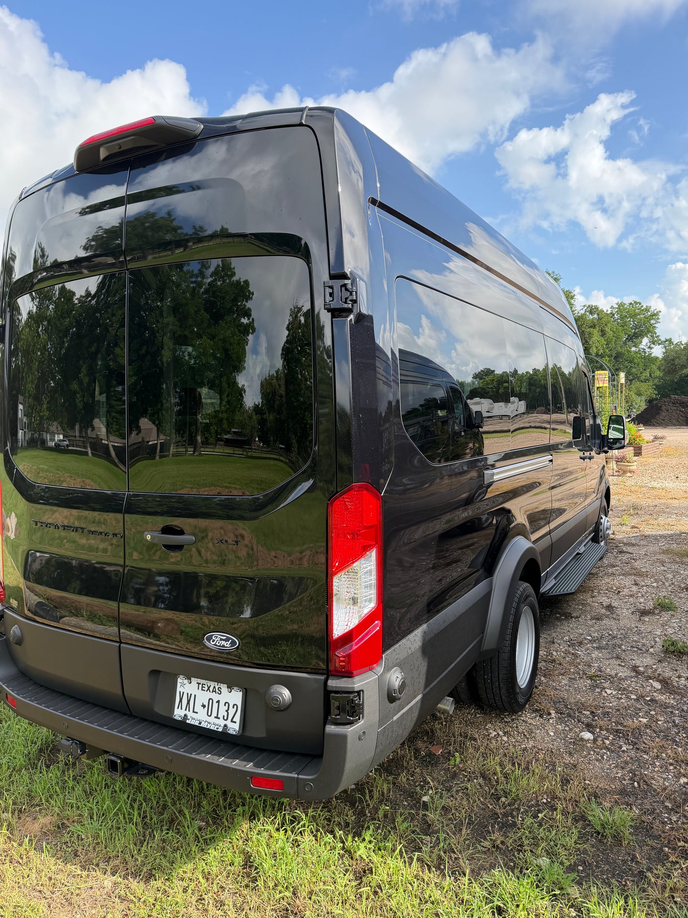 Black Ford Transit van for RV rental, detailed from the rear, reflecting sky & trees on its sleek surface.