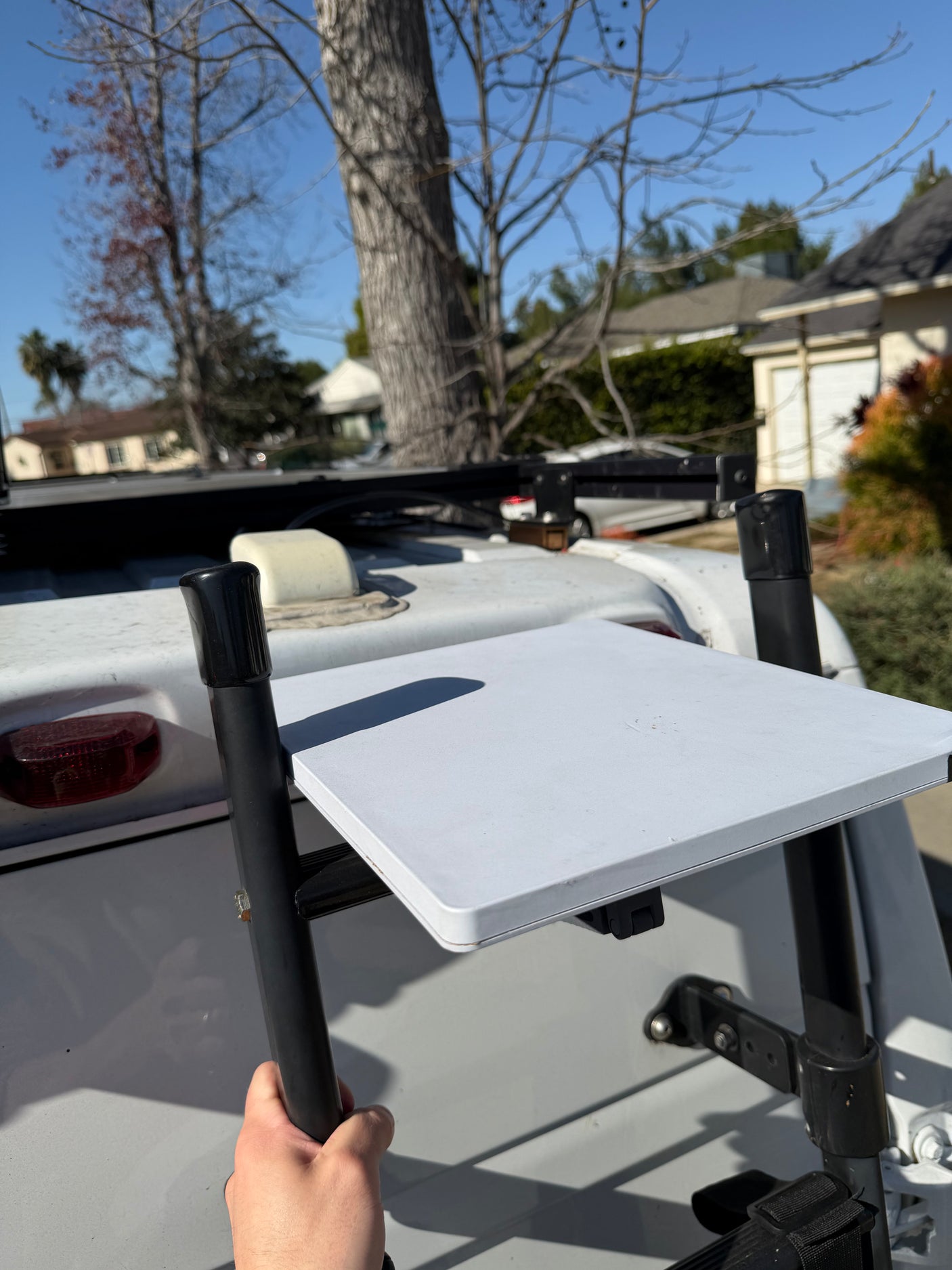 A person's hand adjusts a white, fold-down table attached to the rear of an RV rental, ideal for outdoor tasks or a quick meal.