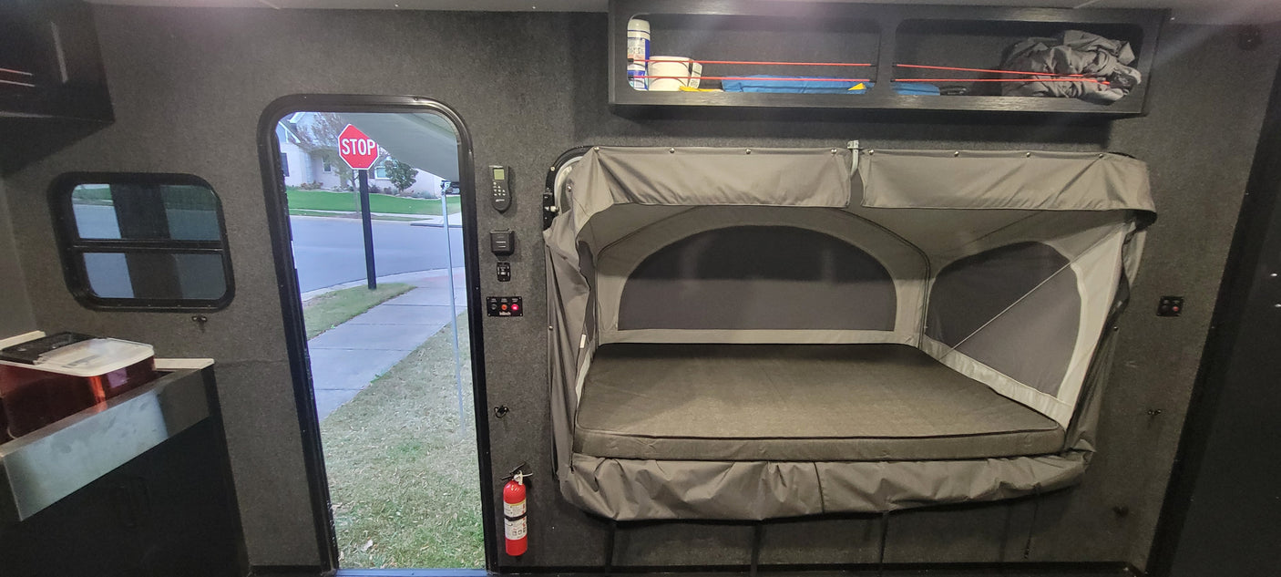 Inside an rv rental: a pop-up bed, controls, window & open door looking at a stop sign on a residential street.