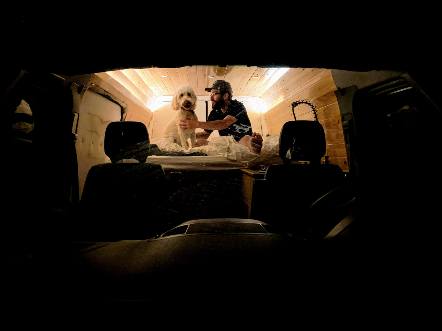 Cozy RV rental interior shows a man and his fluffy dog on a bed with wood paneling, viewed from the driver's seat.
