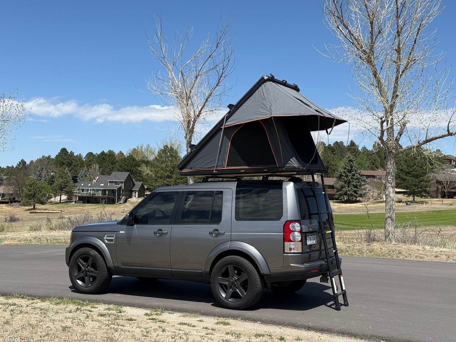 Grey SUV with an open rooftop tent & ladder, parked. An RV rental alternative, perfect for camping and overlanding adventures.