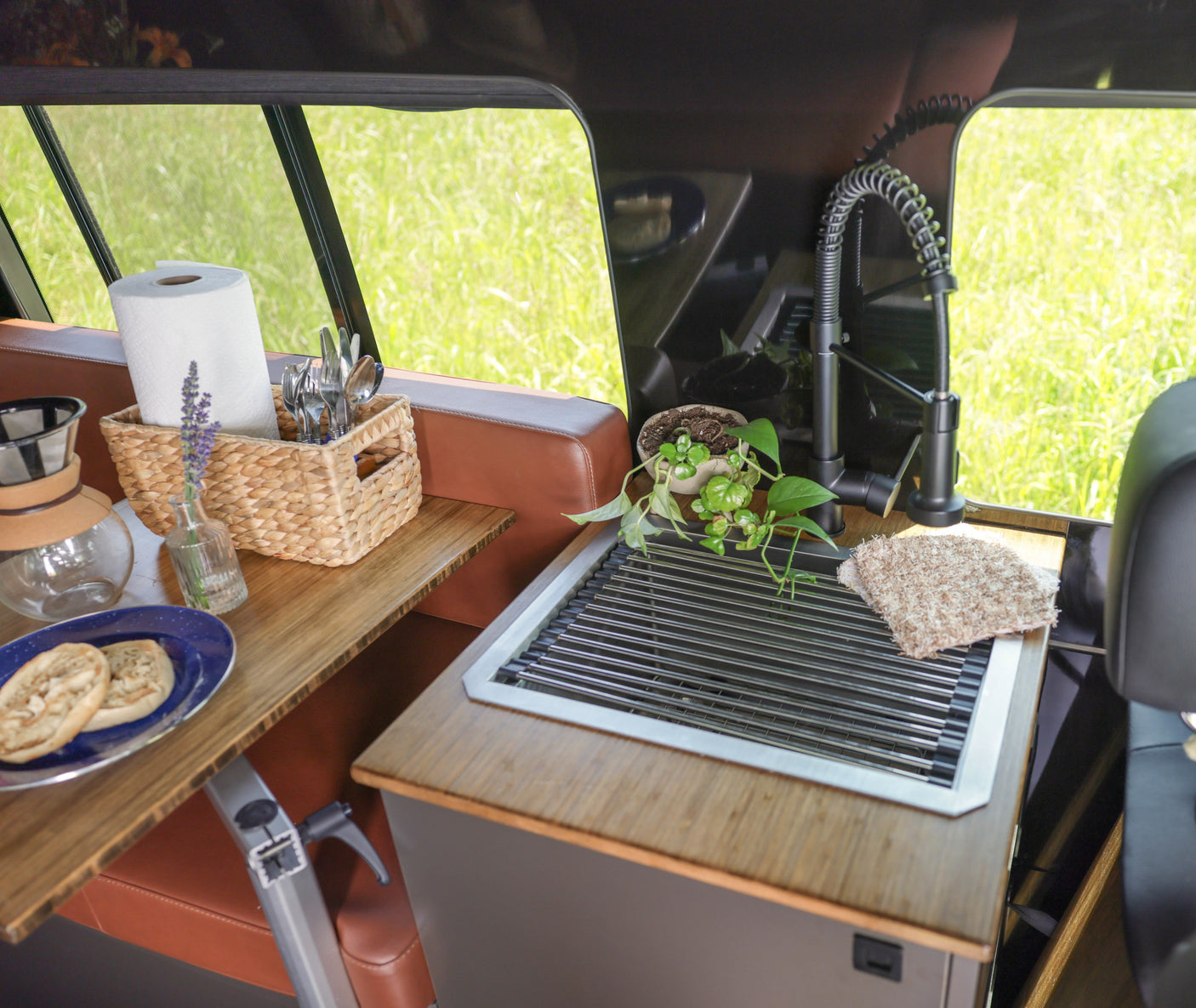 This RV rental features a compact kitchen with a sink, faucet, breakfast bagels, coffee maker, and a green outdoor view.