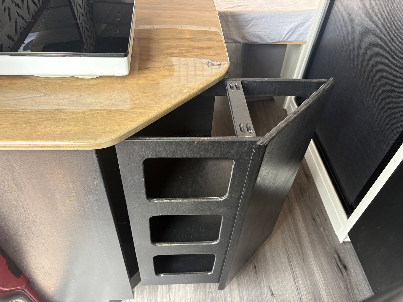 RV rental interior featuring a compact kitchenette on a wooden counter, a black open storage unit, and an adjacent bed.