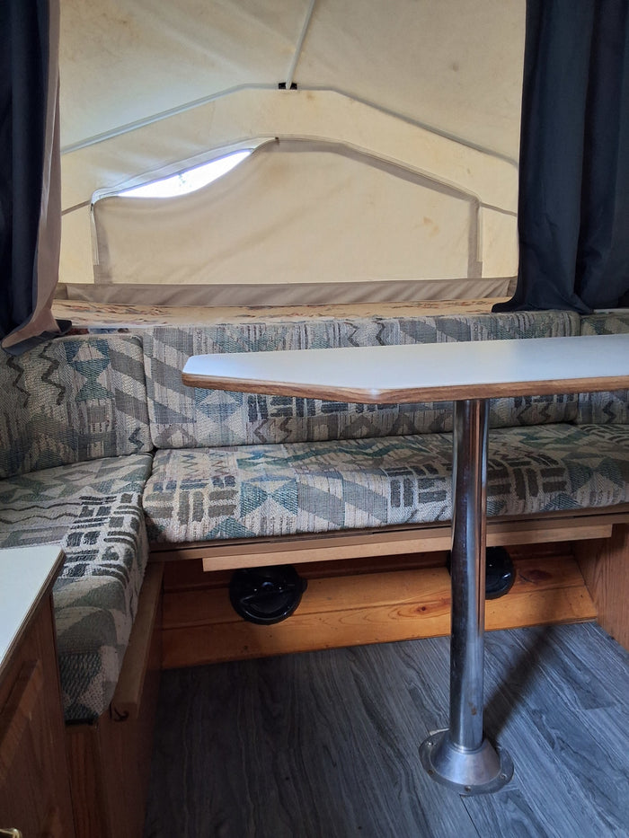Inside an RV rental: view of the dining area with patterned fabric booth seats, a white table, and soft tent walls.