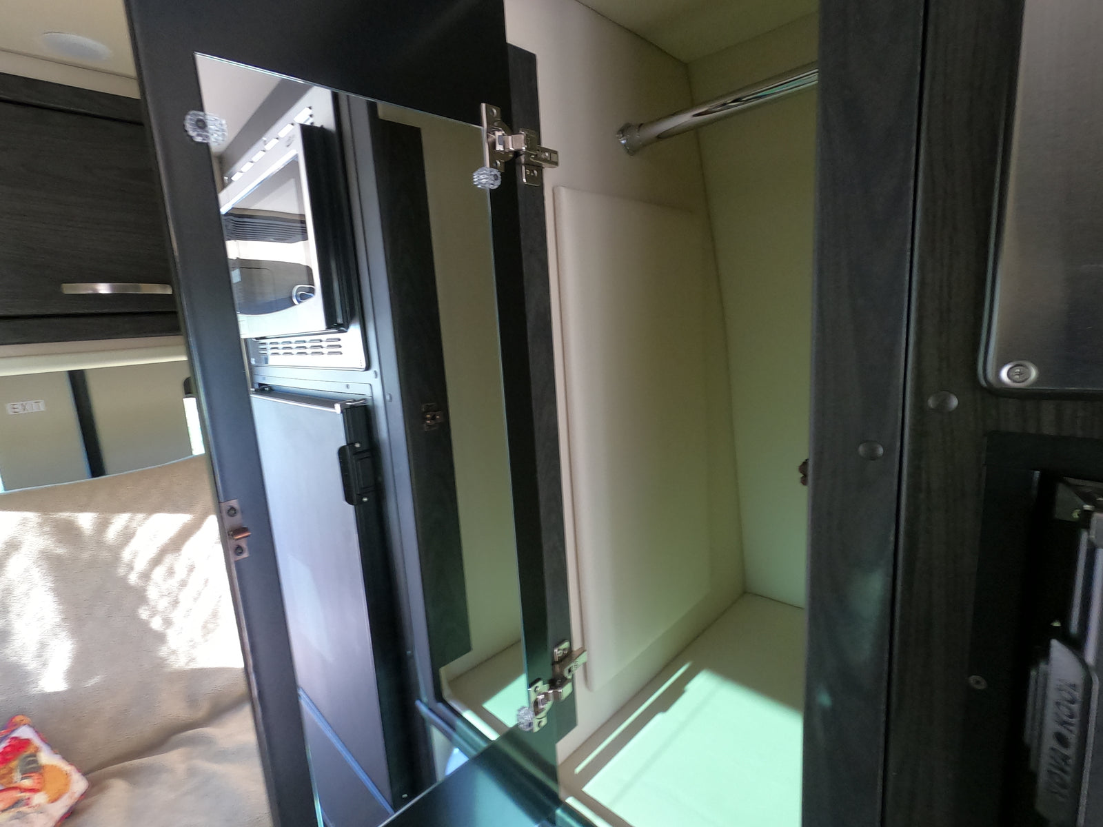 Compact rv rental interior with an open wardrobe and hanging bar, reflecting a view of the microwave, fridge, and seating area.