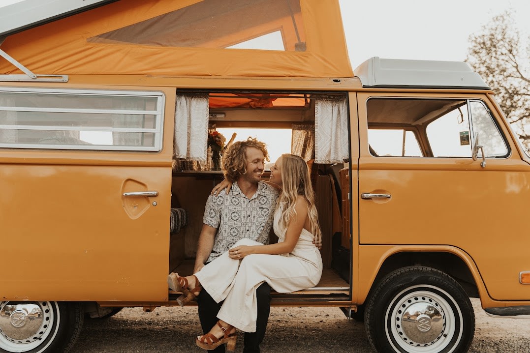 Couple smiles inside their orange vintage camper van RV rental, ready for adventure.