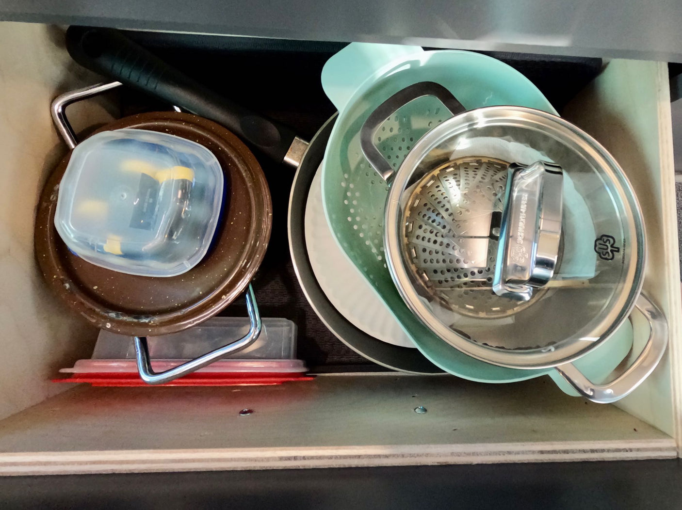 Organized kitchen drawer in an RV rental: pan, colander, pot, plates, & containers. Space-saving storage for camping.