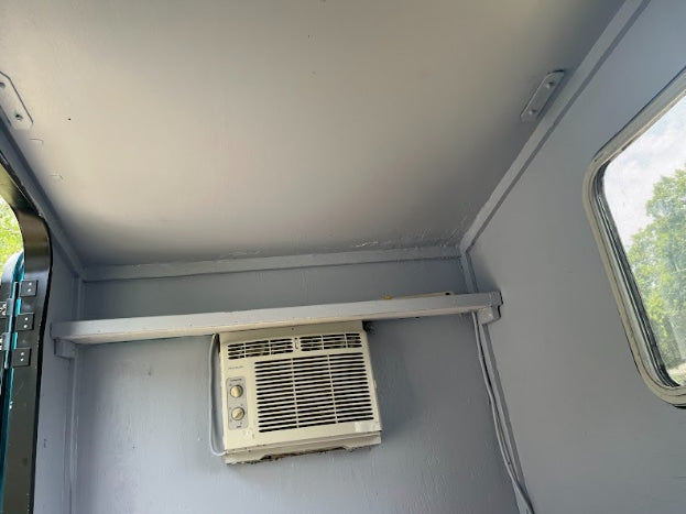 View of an RV rental's grey interior with a mounted AC unit, shelf, and window.