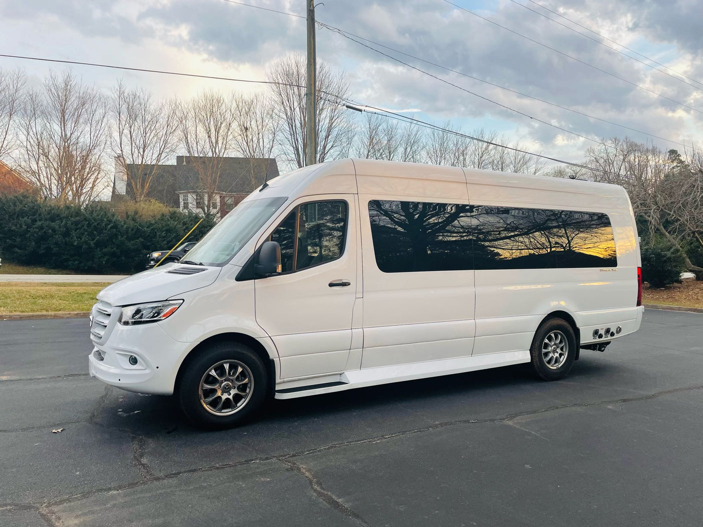 Spacious white Mercedes Sprinter RV rental van parked on asphalt. Reflections of trees & sunset in windows. Adventure awaits!