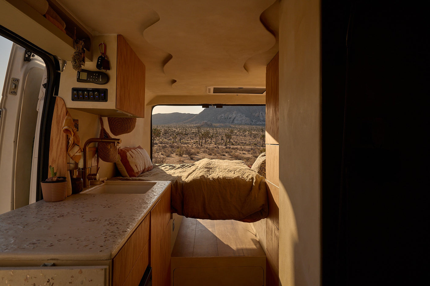 Cozy RV rental interior: A modern camper van with a bed, kitchen, and a desert view through the back window.