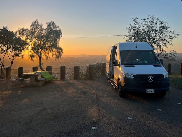 Golden hour illuminates an rv rental parked at a scenic overlook, offering stunning city views alongside a picnic table for travelers.