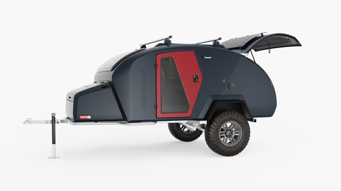 Dark blue Escapod TOPO 2 teardrop camper trailer with red door, solar panels, and off-road tires, great for RV rental.