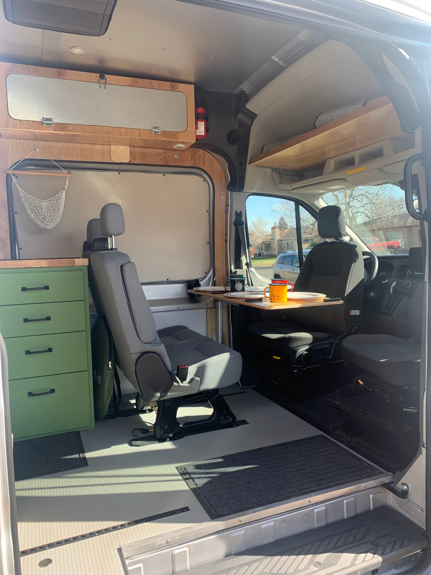 View inside an RV rental van: custom wood cabinets, front seats, and a versatile gray passenger seat, optimized for mobile living.