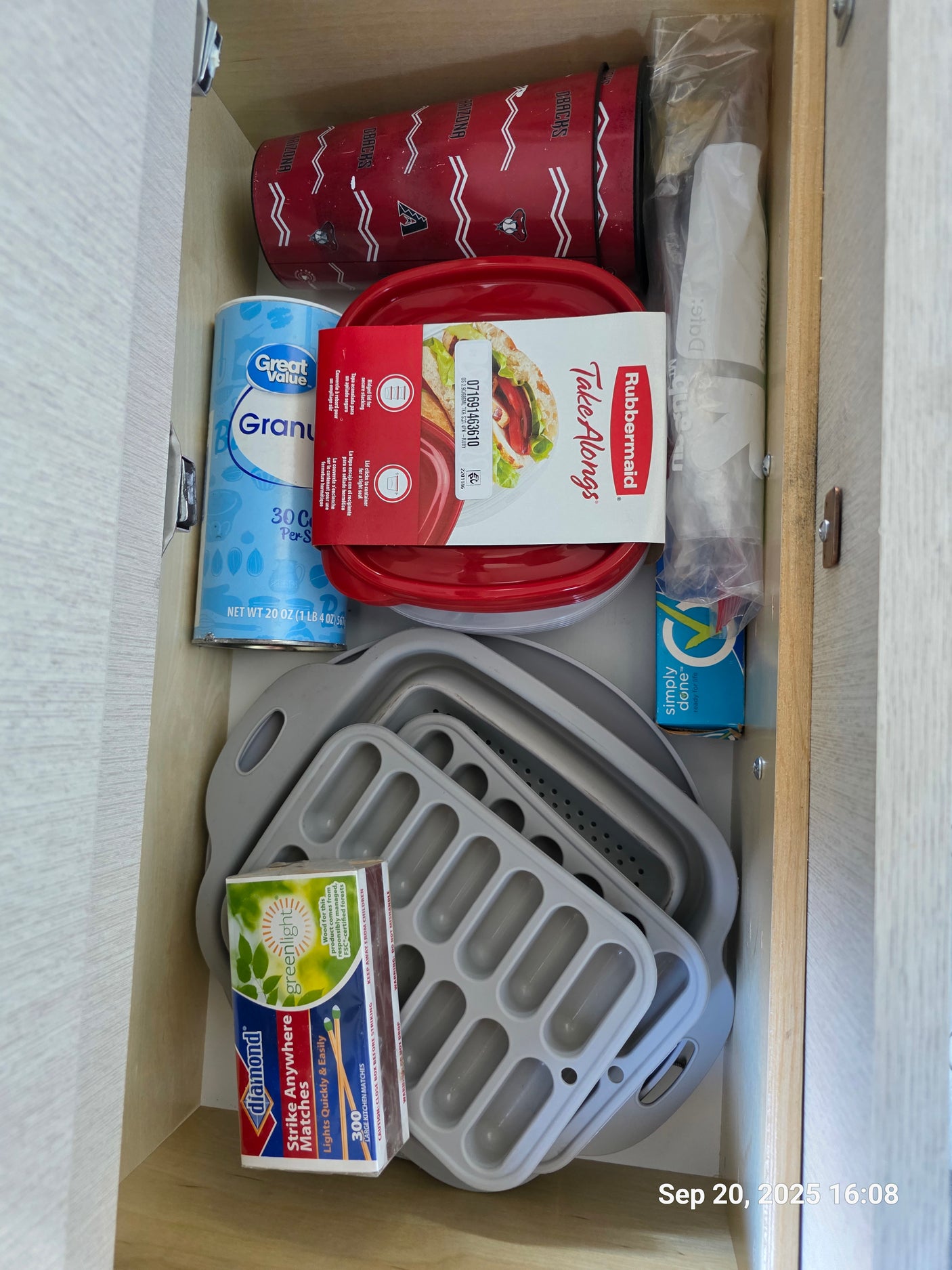 RV rental kitchen drawer with essential camping supplies: matches, food containers, and collapsible kitchenware.
