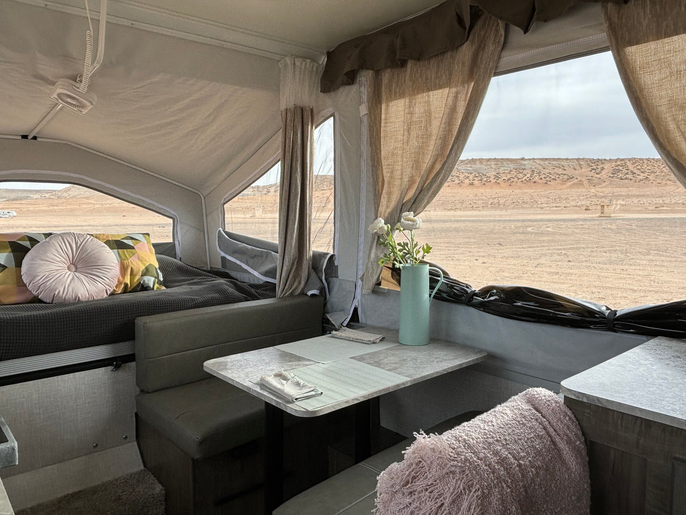 Spacious RV rental interior featuring a dinette, cozy bed, and scenic desert views through large windows.