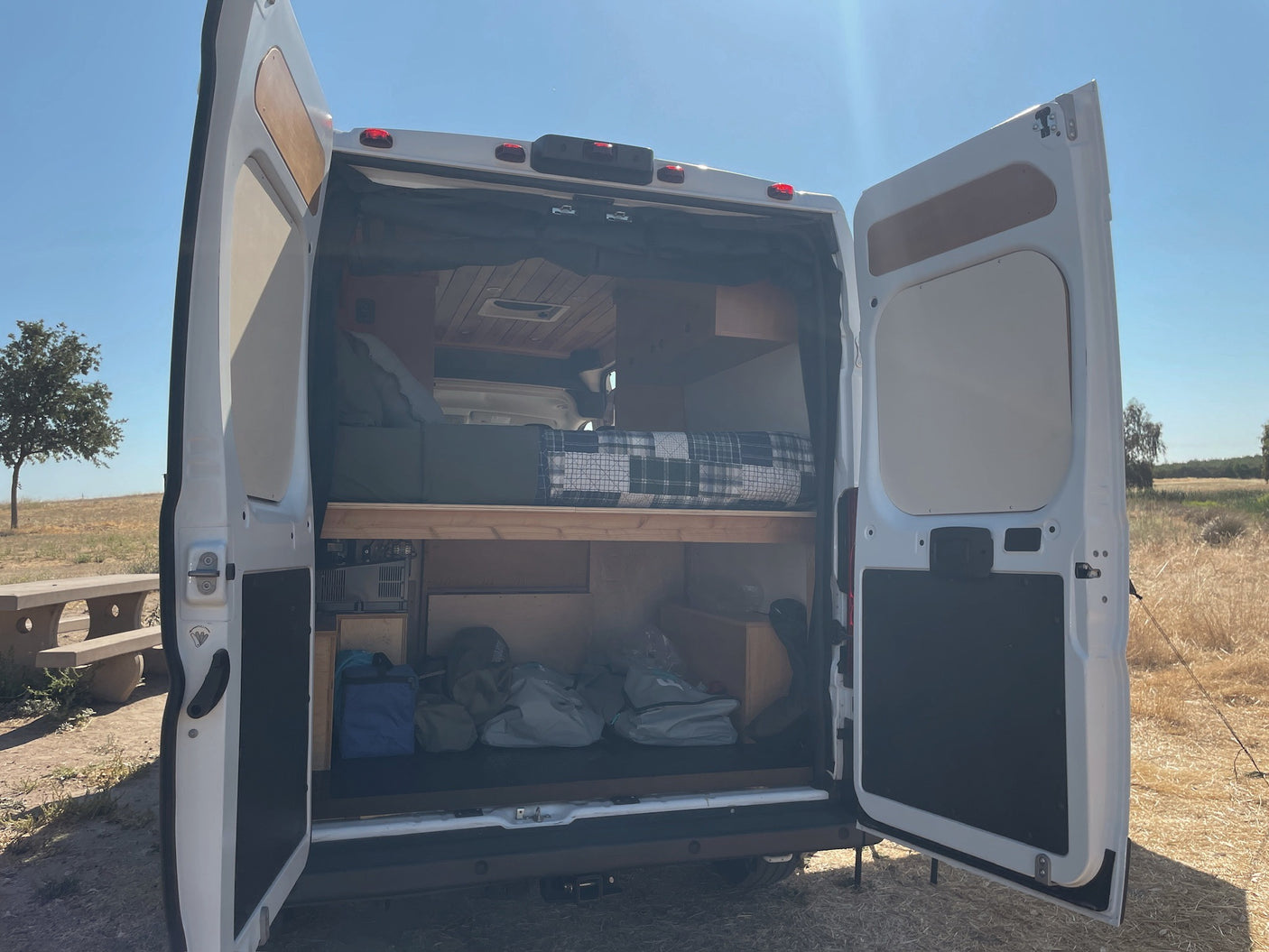 Open rear doors of a white camper van showing its interior bed & storage, ready for adventure. Ideal for an RV rental.